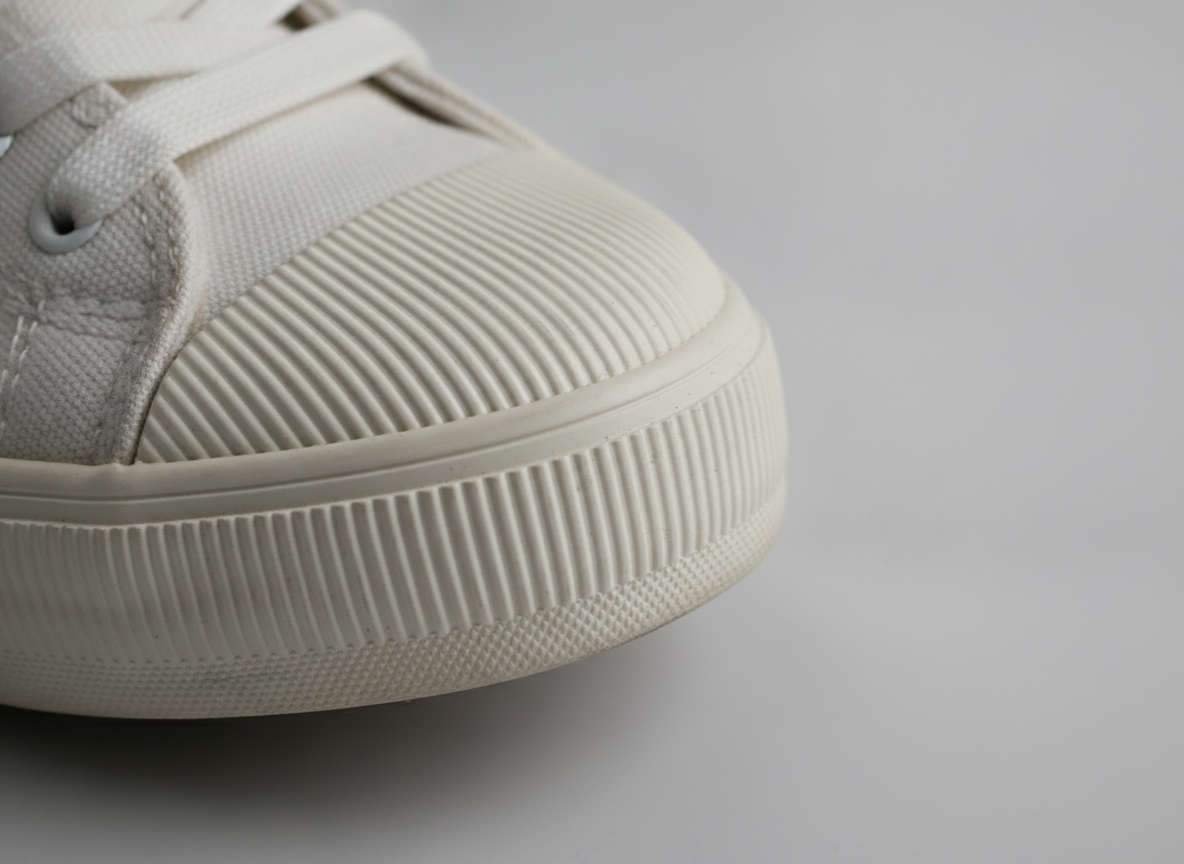 Gros plan sur la shell toe cannelée d'une sneaker basse blanche — détail texture caoutchouc